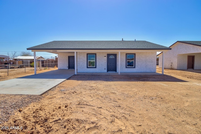 ranch-style home featuring a carport, stucco siding, a shingled roof, and fence