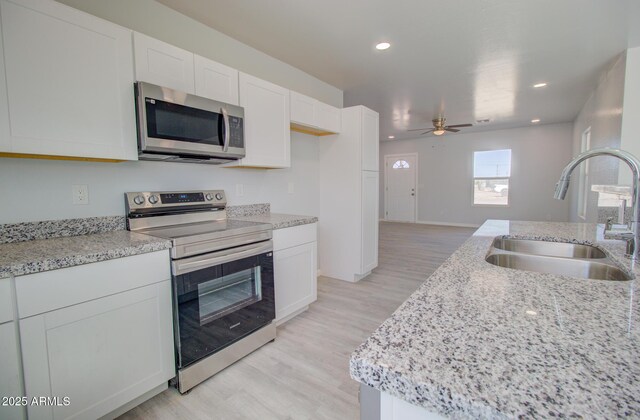 kitchen with ceiling fan, a sink, light wood-style floors, appliances with stainless steel finishes, and white cabinetry