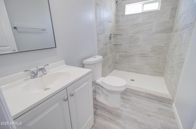 bathroom featuring vanity, toilet, wood finished floors, and tiled shower