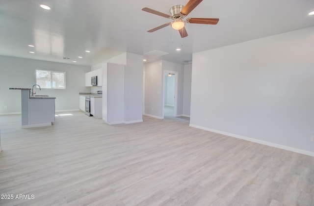 unfurnished living room with recessed lighting, light wood-type flooring, baseboards, and a sink