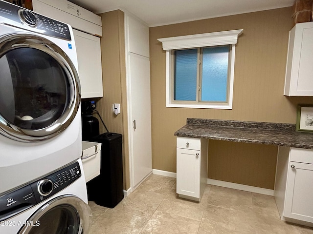 laundry area featuring stacked washer / drying machine and cabinets