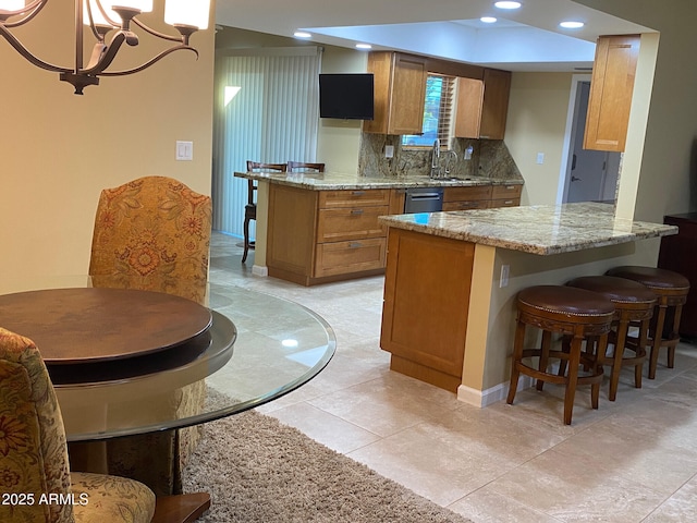 kitchen with an inviting chandelier, sink, decorative backsplash, light stone counters, and kitchen peninsula