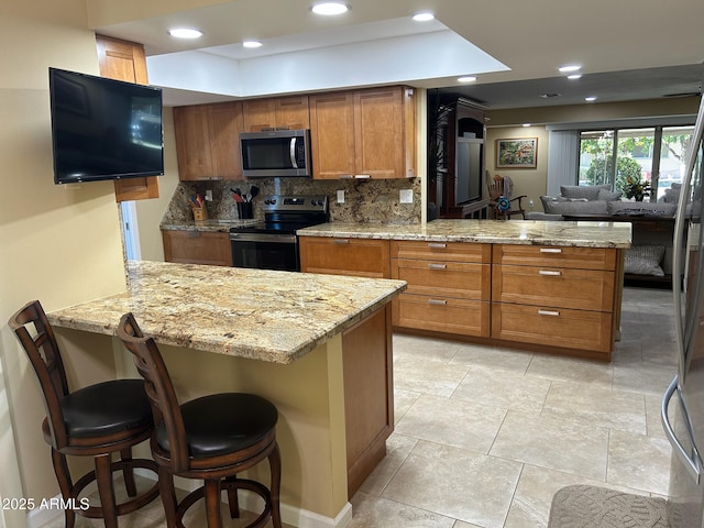 kitchen with stainless steel appliances, tasteful backsplash, light stone counters, kitchen peninsula, and a breakfast bar