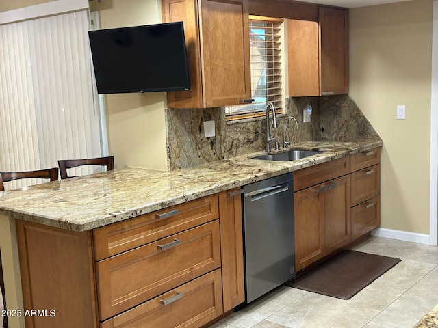 kitchen featuring dishwasher, sink, light stone counters, a kitchen bar, and decorative backsplash