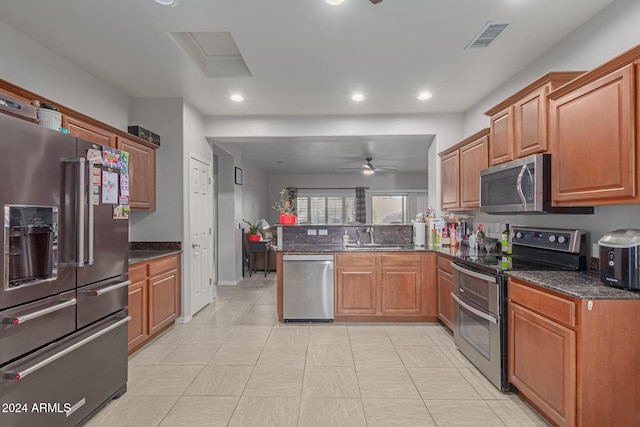 kitchen featuring stainless steel appliances, sink, dark stone countertops, kitchen peninsula, and ceiling fan