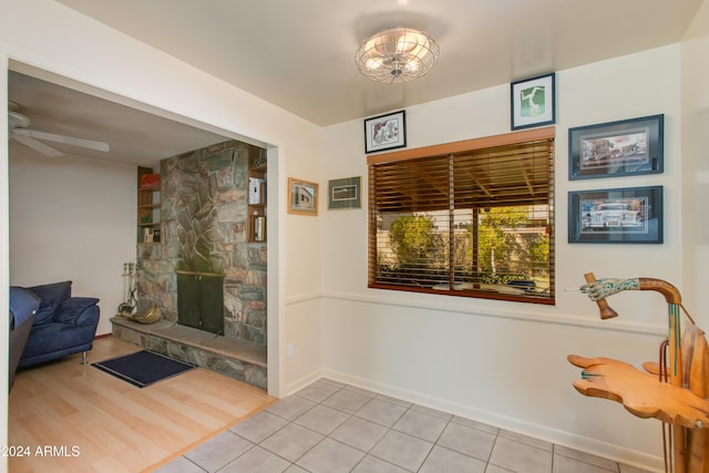 living area featuring light tile patterned flooring, ceiling fan, and a stone fireplace