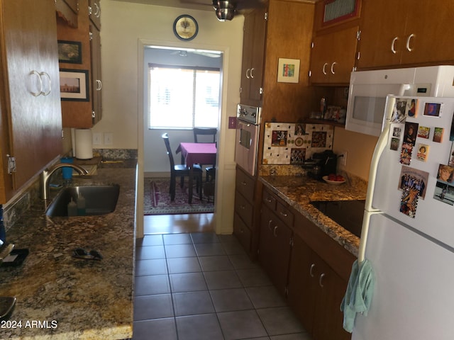 kitchen featuring sink, white refrigerator, tile patterned floors, dark stone counters, and stainless steel oven