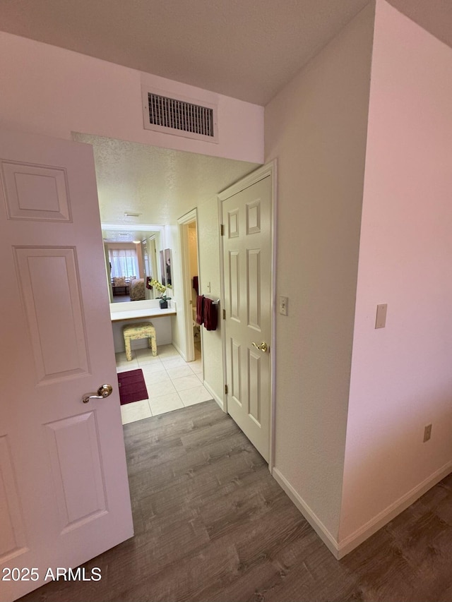 corridor featuring visible vents, baseboards, and wood finished floors