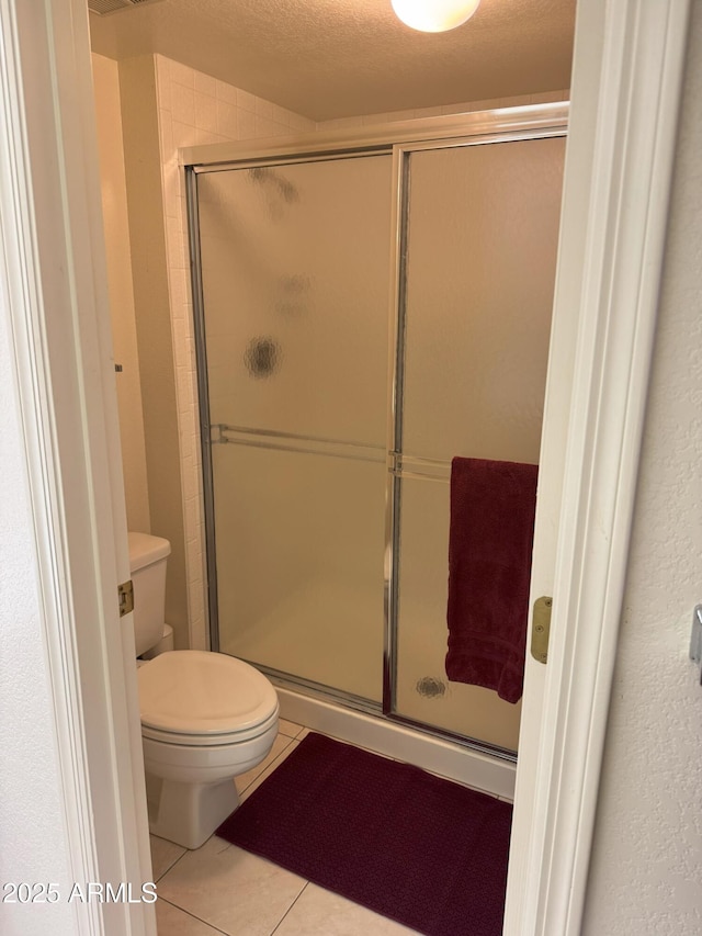 full bathroom with tile patterned floors, toilet, a stall shower, and a textured ceiling