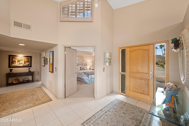 foyer entrance with a high ceiling, light tile patterned floors, baseboards, and visible vents