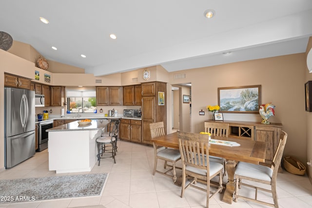 kitchen featuring brown cabinets, a sink, a center island, stainless steel appliances, and vaulted ceiling