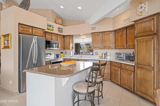 kitchen with visible vents, a kitchen island, light tile patterned floors, appliances with stainless steel finishes, and brown cabinetry