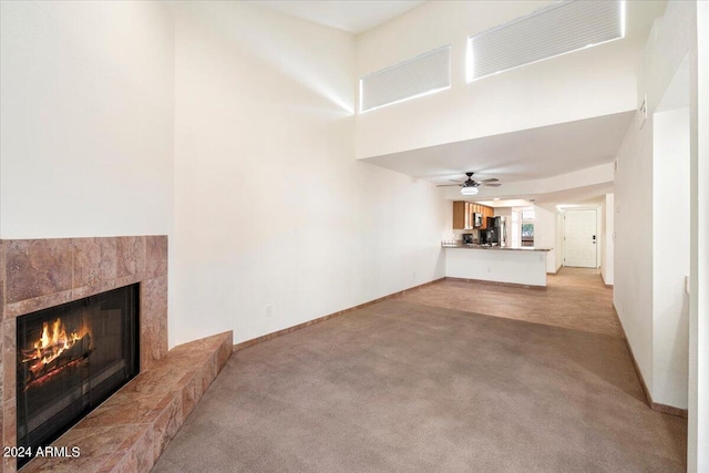 unfurnished living room featuring ceiling fan, light carpet, and a tile fireplace