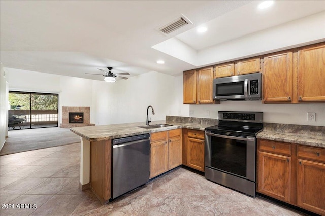 kitchen with kitchen peninsula, appliances with stainless steel finishes, ceiling fan, sink, and a fireplace