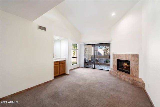 unfurnished living room with a tiled fireplace, high vaulted ceiling, and light colored carpet