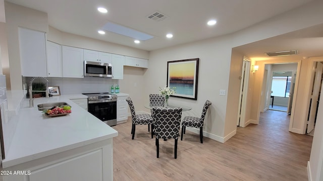 kitchen with decorative backsplash, appliances with stainless steel finishes, sink, light hardwood / wood-style flooring, and white cabinetry