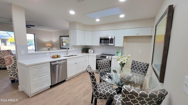 kitchen featuring tasteful backsplash, stainless steel appliances, sink, light hardwood / wood-style floors, and white cabinetry