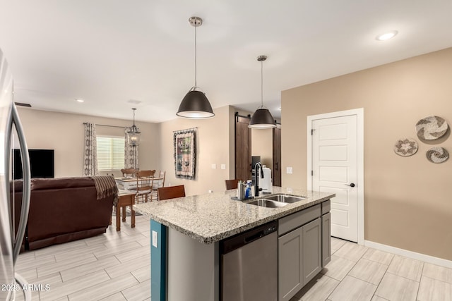 kitchen featuring gray cabinets, an island with sink, appliances with stainless steel finishes, decorative light fixtures, and sink