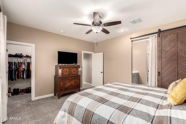 bedroom with ensuite bathroom, a barn door, ceiling fan, a walk in closet, and a closet