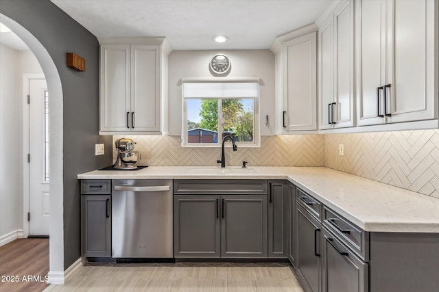 kitchen featuring dishwasher, gray cabinets, arched walkways, and a sink