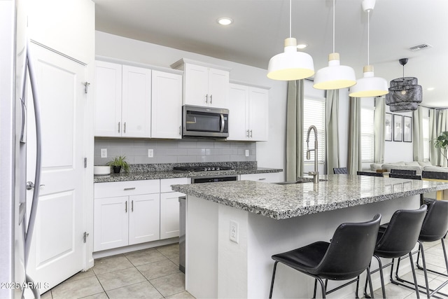 kitchen featuring light tile patterned floors, a breakfast bar, a sink, appliances with stainless steel finishes, and tasteful backsplash