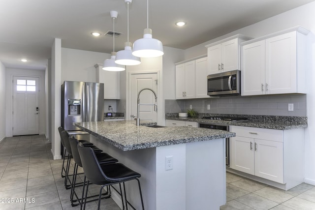 kitchen featuring stainless steel appliances, visible vents, backsplash, a kitchen island with sink, and a sink