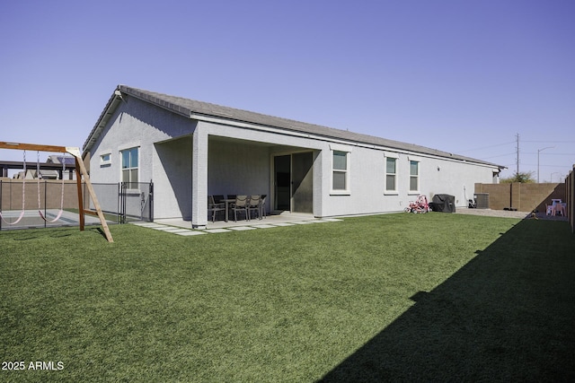 rear view of property featuring a patio, fence, a lawn, and stucco siding