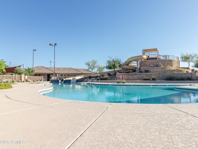 community pool featuring a patio, a water slide, and fence