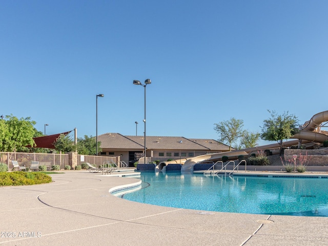 community pool featuring a patio area, fence, and a water slide