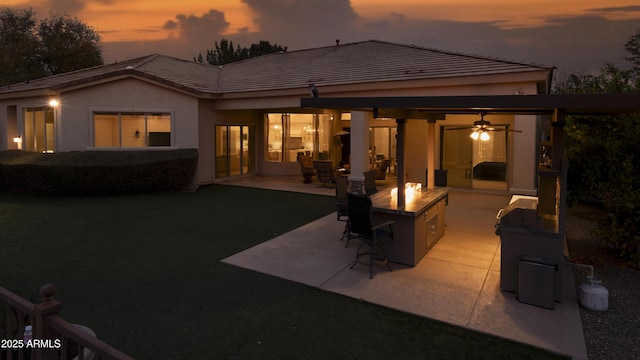 back house at dusk with ceiling fan, an outdoor fire pit, and a patio area