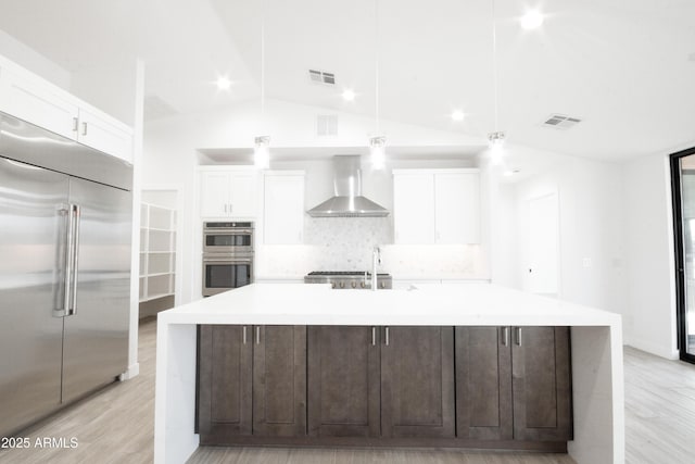 kitchen with decorative backsplash, stainless steel appliances, a kitchen island with sink, and wall chimney exhaust hood