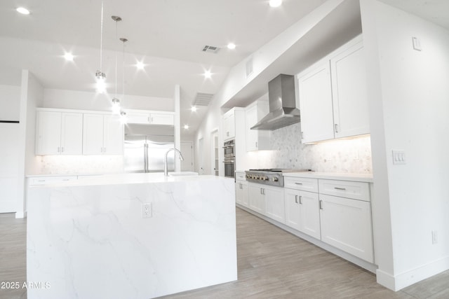 kitchen with white cabinets, wall chimney range hood, a large island with sink, and appliances with stainless steel finishes