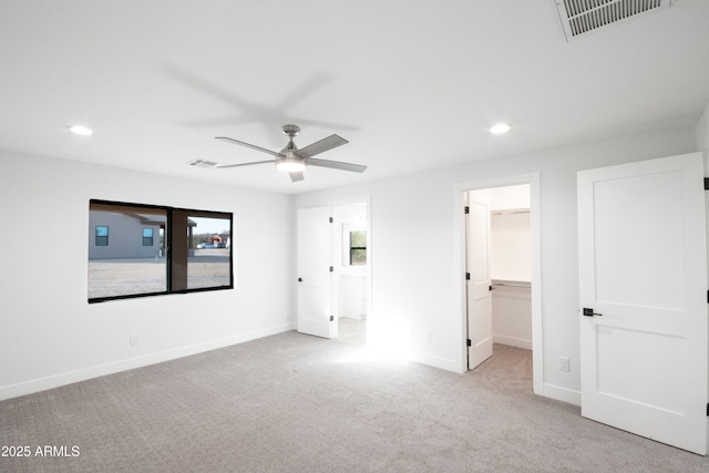 unfurnished bedroom featuring a walk in closet, ceiling fan, a closet, and light colored carpet