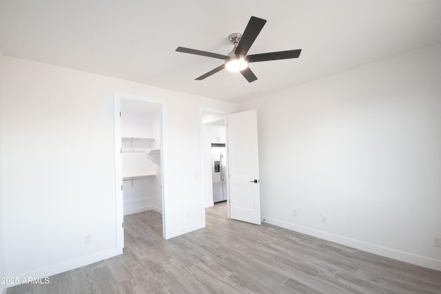 unfurnished bedroom with ceiling fan, stainless steel fridge with ice dispenser, light hardwood / wood-style flooring, a walk in closet, and a closet