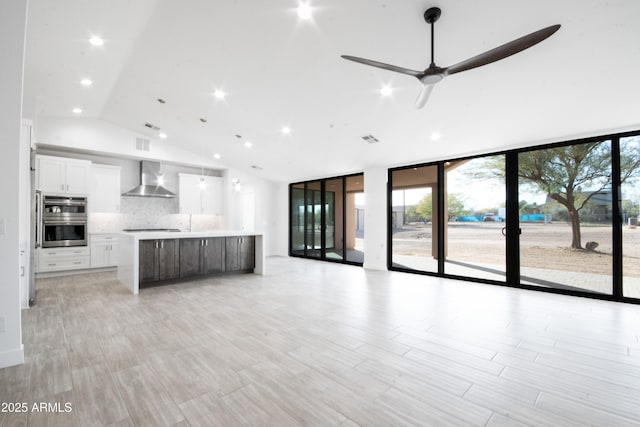 kitchen with pendant lighting, a center island, backsplash, white cabinets, and wall chimney range hood