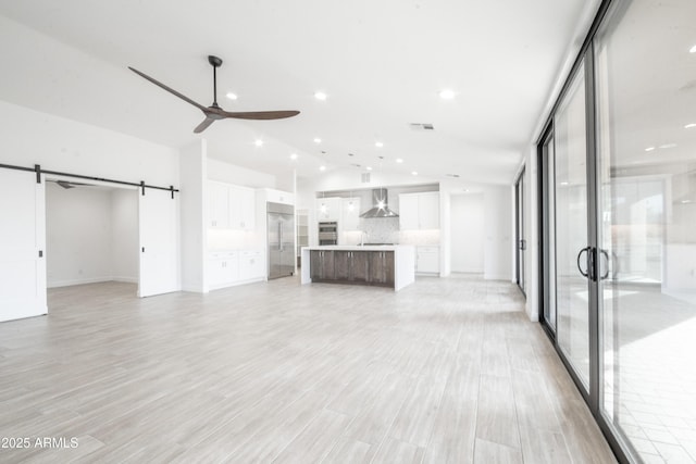 unfurnished living room with sink, vaulted ceiling, ceiling fan, a barn door, and light hardwood / wood-style floors