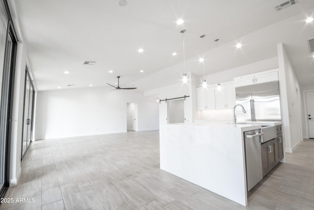 kitchen with appliances with stainless steel finishes, a barn door, white cabinets, hanging light fixtures, and an island with sink