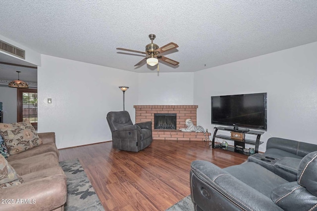 living room with hardwood / wood-style flooring, ceiling fan, a fireplace, and a textured ceiling