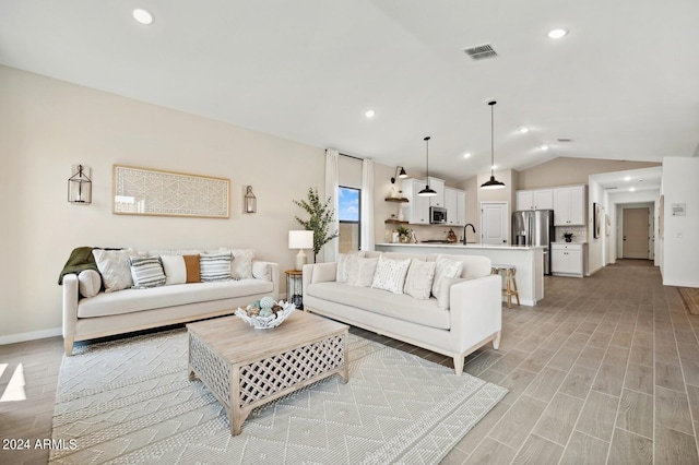 living room with sink, light hardwood / wood-style floors, and vaulted ceiling