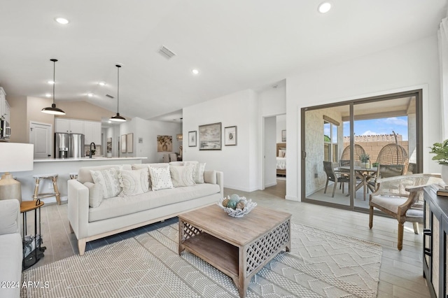 living room with sink, light wood-type flooring, and vaulted ceiling