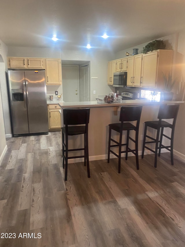 kitchen featuring appliances with stainless steel finishes, kitchen peninsula, a kitchen breakfast bar, and dark hardwood / wood-style floors