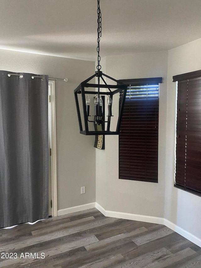 unfurnished dining area featuring an inviting chandelier and dark wood-type flooring