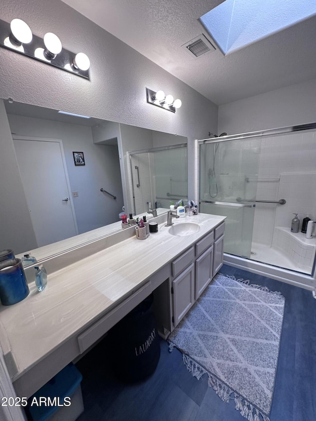 bathroom featuring vanity, an enclosed shower, a textured ceiling, and a skylight