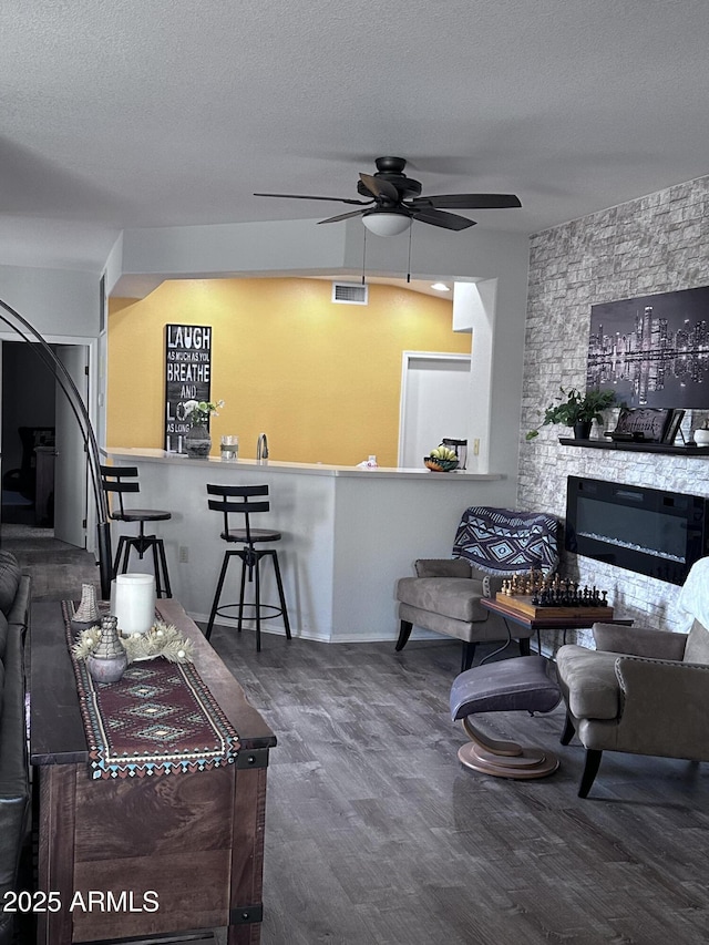 living room featuring ceiling fan, a fireplace, hardwood / wood-style floors, and a textured ceiling