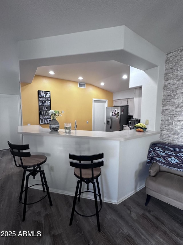 kitchen with stainless steel refrigerator with ice dispenser, a breakfast bar area, white cabinetry, dark hardwood / wood-style floors, and kitchen peninsula