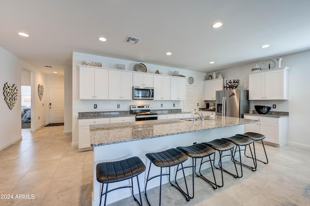 kitchen with stainless steel appliances, white cabinetry, and a center island with sink