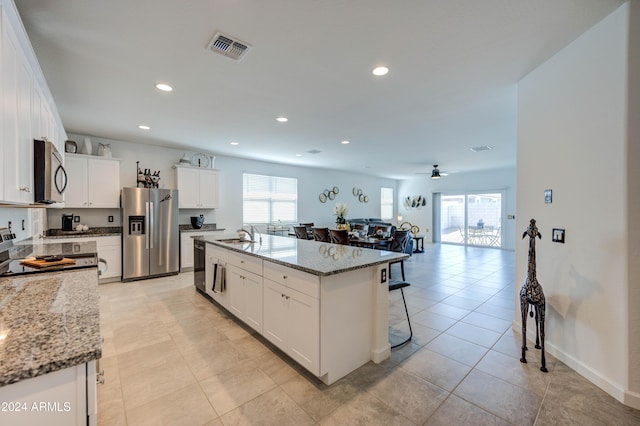 kitchen featuring light stone counters, an island with sink, white cabinets, and appliances with stainless steel finishes