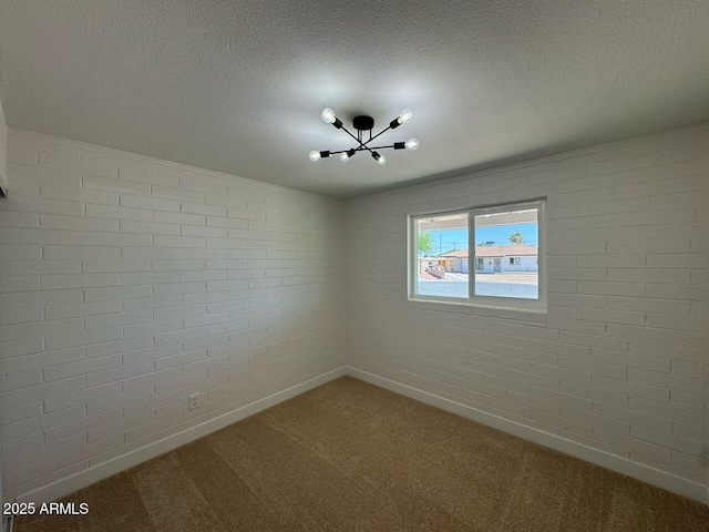 unfurnished room featuring a textured ceiling, carpet flooring, a notable chandelier, and baseboards