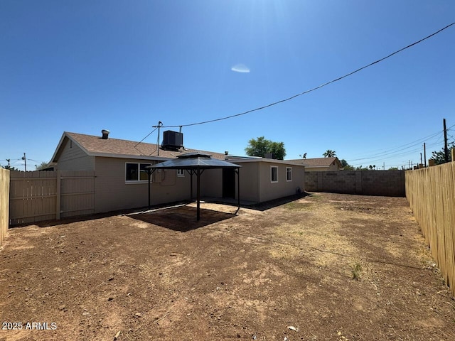 rear view of property featuring a fenced backyard, a gazebo, and central AC