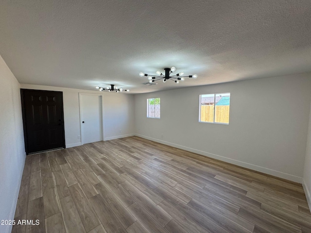 empty room with baseboards, a chandelier, a textured ceiling, and wood finished floors